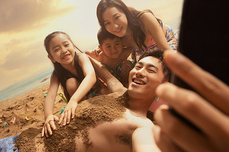 沙滩上男人拿手机和妻子孩子自拍图片