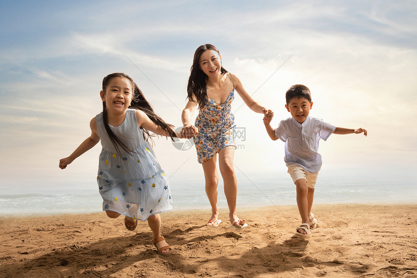 年轻母亲牵着两个孩子在沙滩上奔跑图片