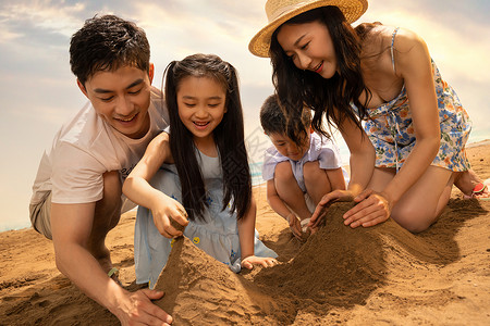 玩沙雕的男孩快乐的四口之家在沙滩上玩沙子背景