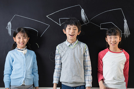 戴博士帽男孩站在黑板前的快乐小学生背景