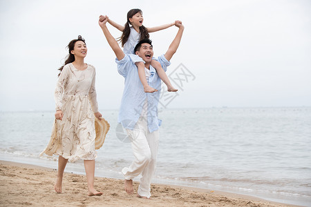 背着孩子父亲幸福的一家三口在海边玩耍背景