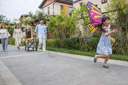 追逐蝴蝶的小女孩拿着风筝的小女孩和家人在户外玩耍背景