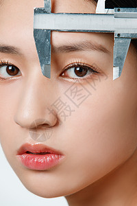 现代美容技术整形医生用卡尺测量青年女人面部背景