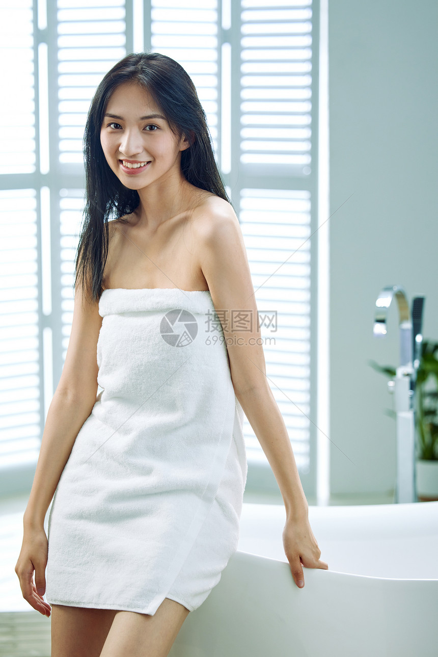 裹着浴巾的青年女人站在浴缸旁图片