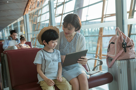 航空包年轻妈妈和儿子在机场候机厅看平板电脑背景