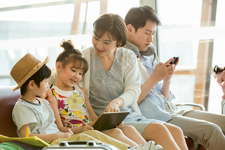 旅游产品快乐家庭在机场候机厅里使用电子产品背景