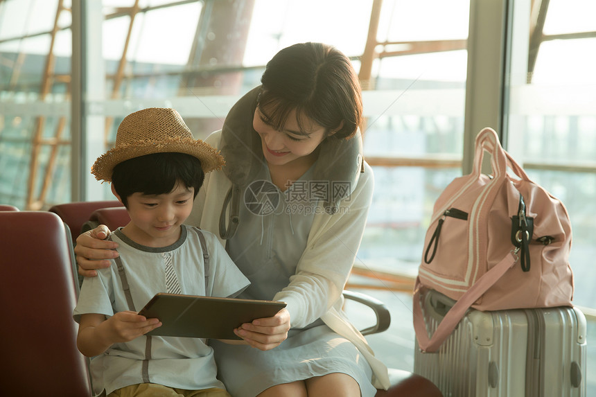 年轻妈妈和儿子在机场候机厅看平板电脑图片