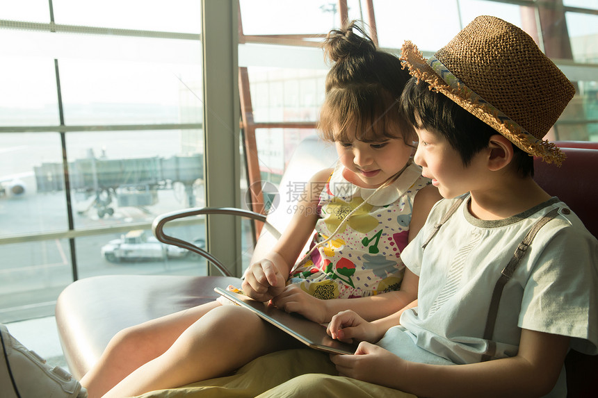 两个小朋友坐在机场候车厅看平板电脑图片