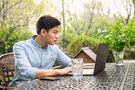 青年男人在院子里用笔记本电脑背景图片
