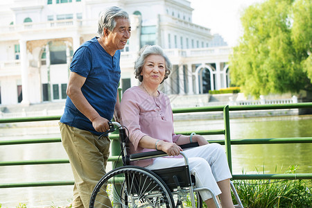 老人户外活动老年人推着坐轮椅的老伴背景