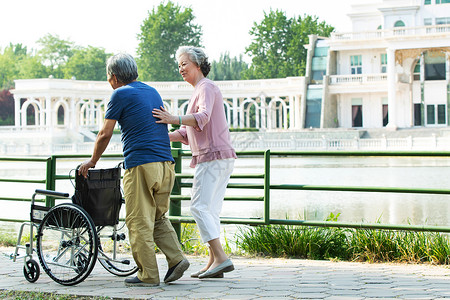 老人户外活动老年人扶着老伴推轮椅背景