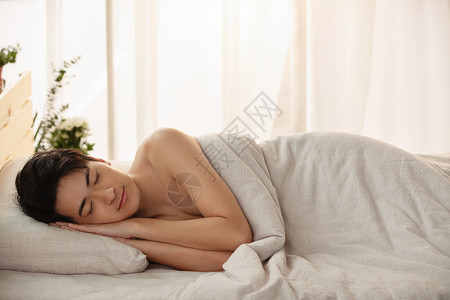 裹着棉被躺在床上睡觉的年轻男人背景