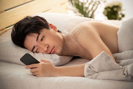 熬夜皮肤躺在床上玩手机的年轻男人背景