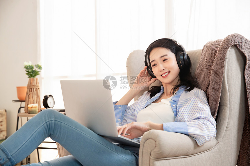 快乐的女青年坐在沙发上使用笔记本电脑图片