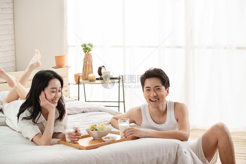 快乐的年轻情侣在床上吃早餐图片