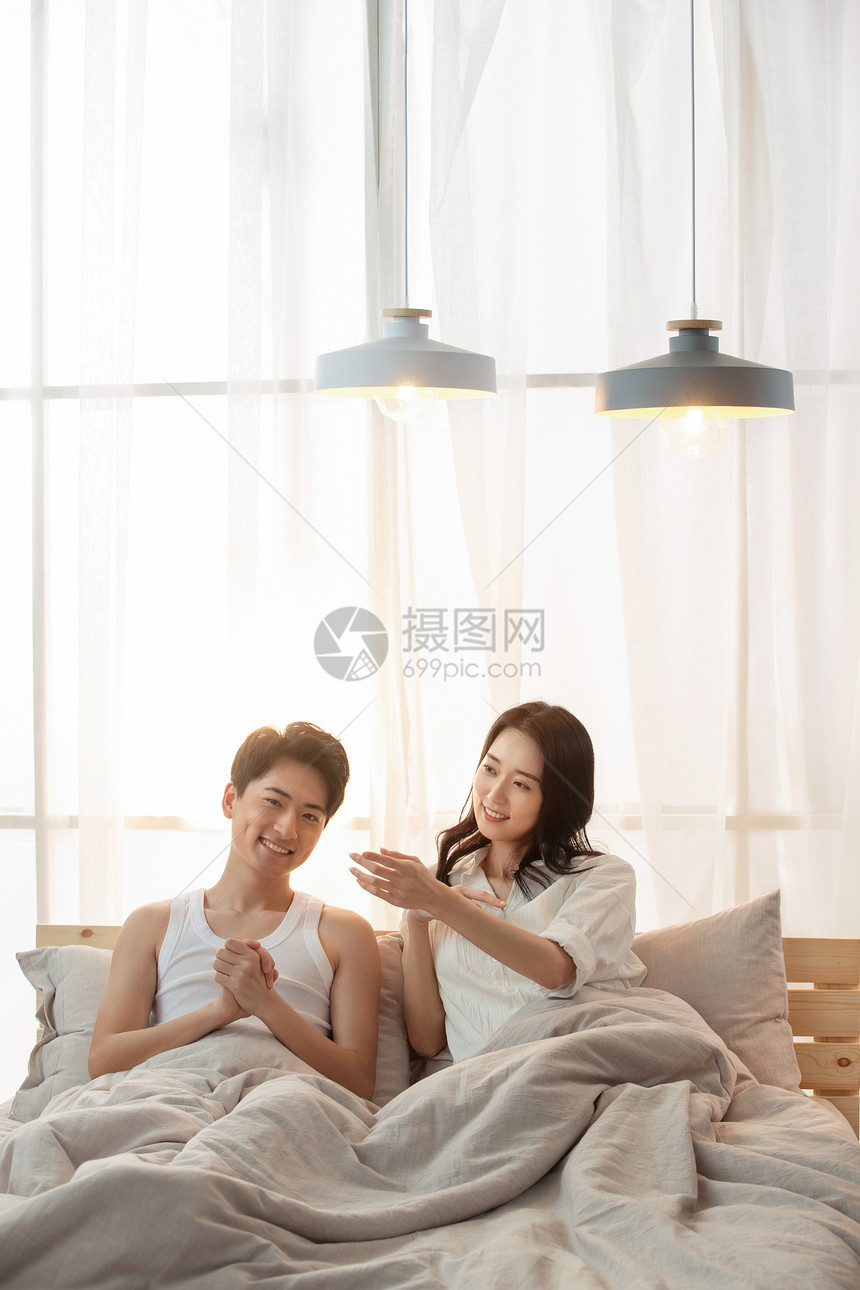 快乐的年轻情侣坐在床上聊天图片