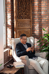 休闲的老年男人坐在沙发上玩手机图片