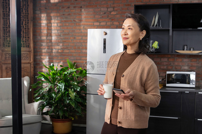 快乐的老年女人拿着手机和牛奶图片