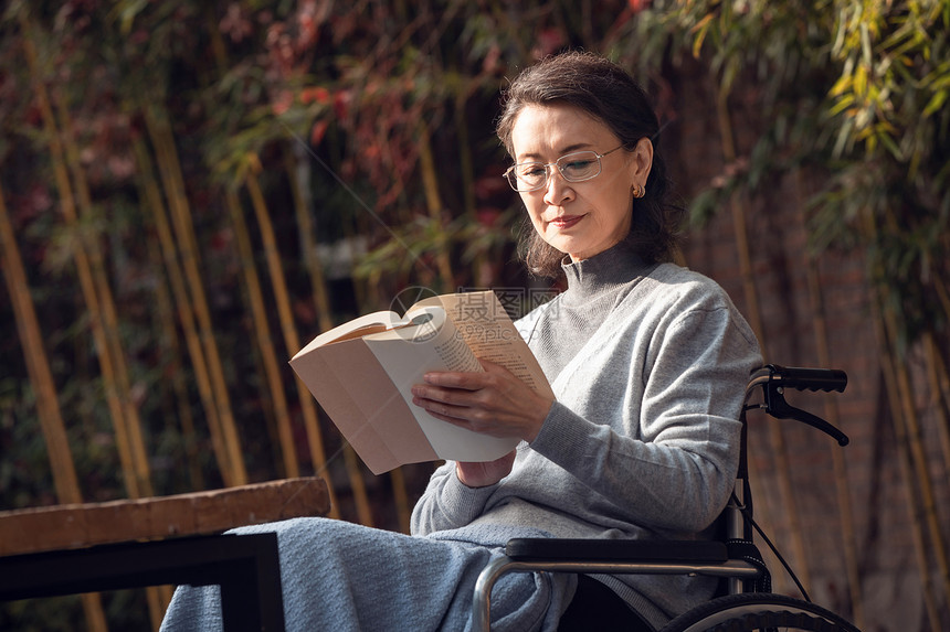 户外老年女人坐在轮椅上看书图片