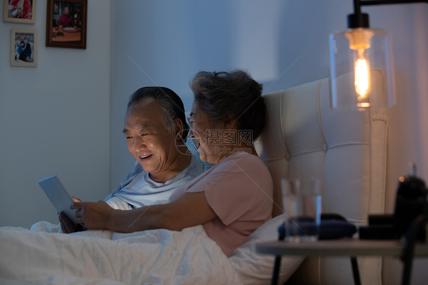 老年夫妇坐在床上用平板电脑看视频图片
