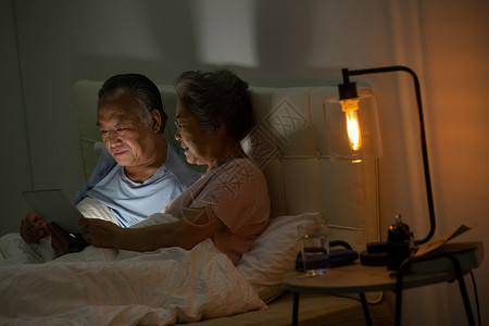 老年夫妇坐在床上用平板电脑看视频高清图片