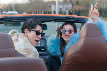 满意的太阳镜时尚的青年伴侣驾驶跑车兜风背景