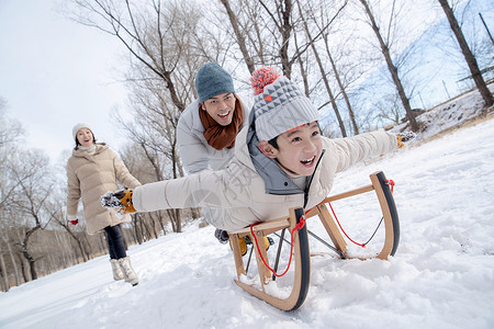 跪在地上的小孩在雪地上玩雪橇的一家人背景