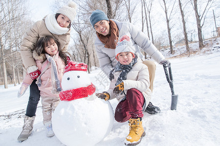 拿着铲子女孩欢乐家庭在雪地里堆雪人背景