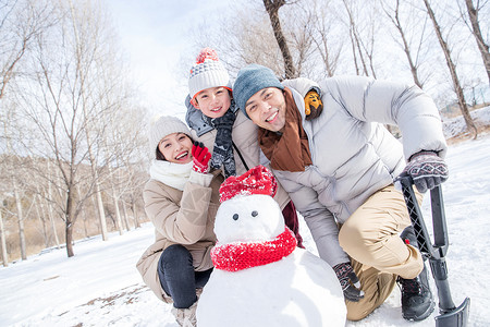 孩子拿着铲子一家三口在雪地里堆雪人背景