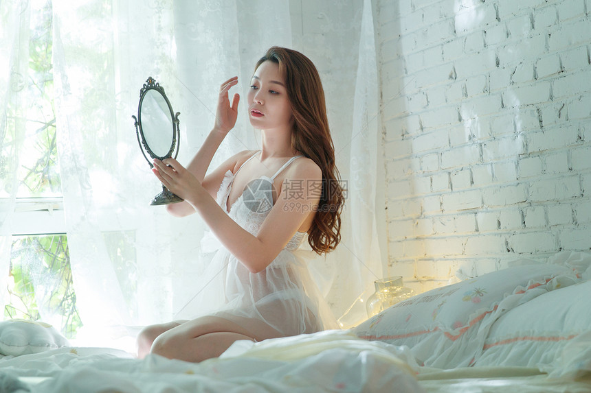 漂亮的青年女人坐在床上照镜子图片