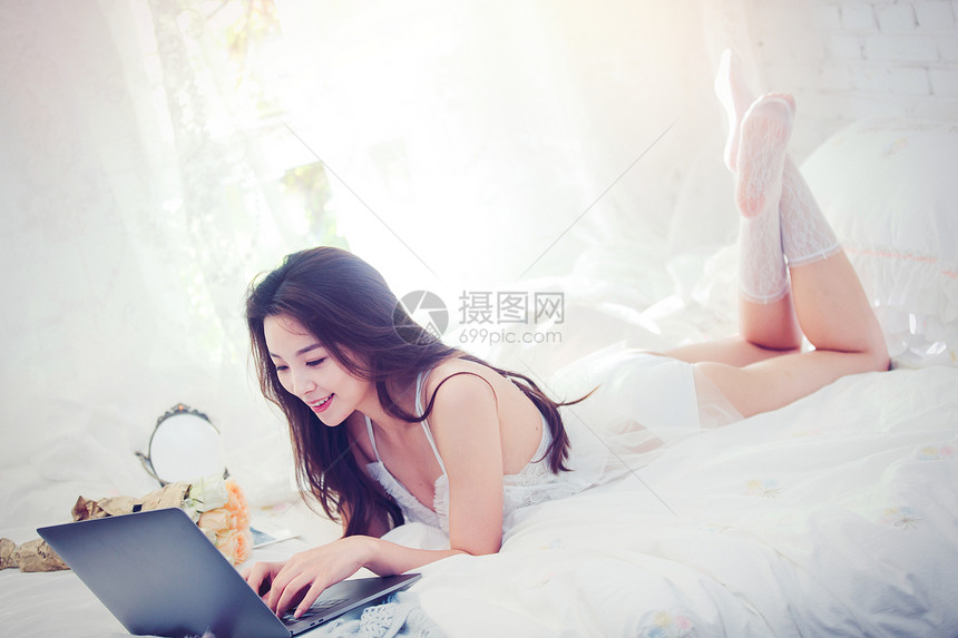 趴在床上使用笔记本电脑的年轻女人图片