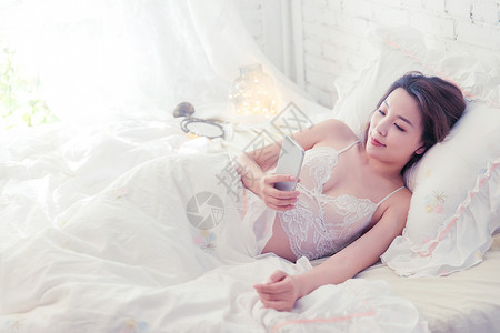 透明飘纱素材青年女人躺在床上使用手机背景