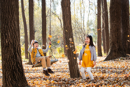 快乐的女孩往荡秋千上的男孩身上抛树叶图片