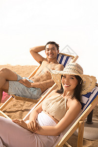坐在沙滩椅上吃西瓜的情侣浪漫的年轻情侣在沙滩上背景