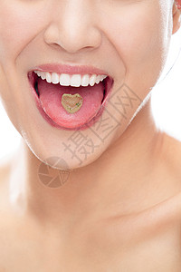 舌头上有颗心形糖的青年女人嘴部特写图片