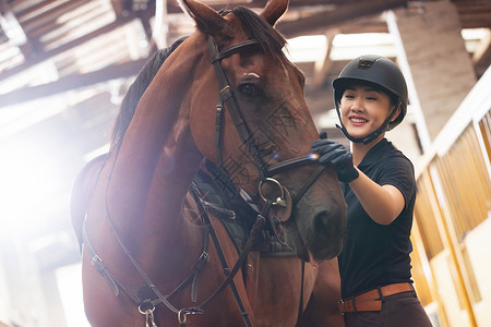 职业赛马骑师马厩里安抚马的年轻女子背景