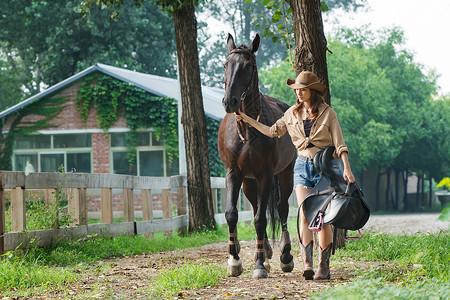 马场内青年女人拿着马具牵着马图片