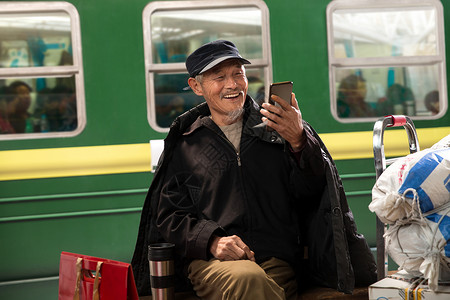 视频短信在火车站台上用手机的老人背景
