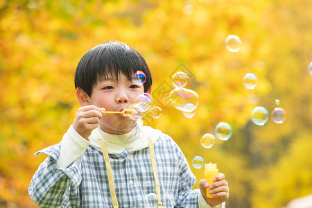 黄色泡泡可爱的小男孩在公园里吹泡泡背景