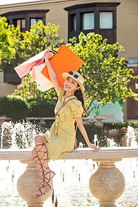 遮阳帽图片拿着购物袋的年轻女人坐在喷泉边背景