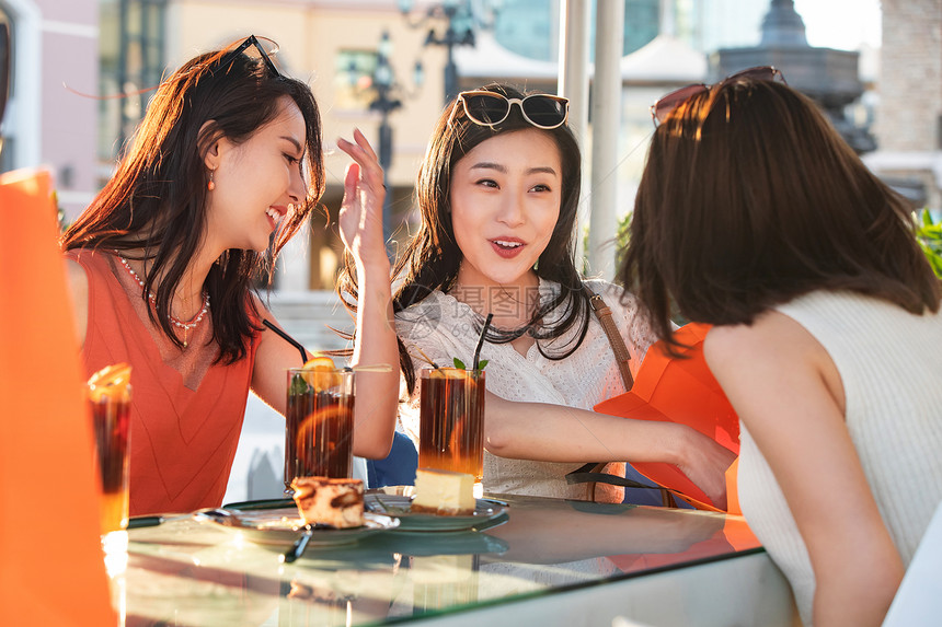 快乐的青年女人们坐在露天咖啡馆分享购物成果图片