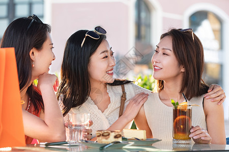 漂亮年轻的女孩们坐在路边咖啡馆聊天背景图片