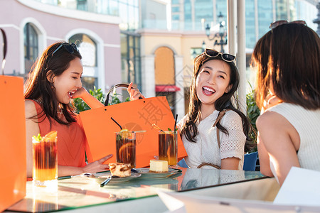 分享成果快乐的青年女人们坐在露天咖啡馆分享购物成果背景