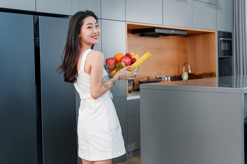 拿着水果的青年女人站在冰箱前图片