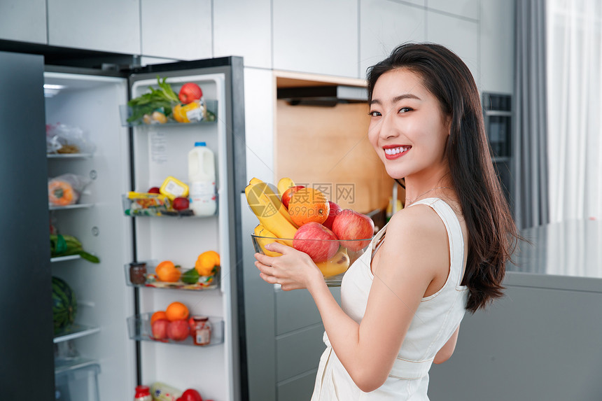 拿着水果的青年女人站在冰箱前图片