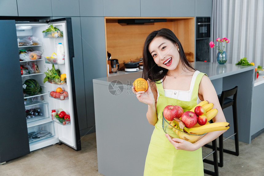 拿着水果的青年女人站在冰箱前图片