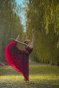 向上伸展穿红色裙子的青年女人在户外跳芭蕾舞背景
