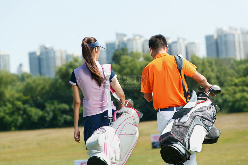 青年人背着高尔夫球包在球场行走的背影图片