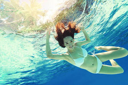 漂亮连体的泳衣年轻女人在水下游泳背景