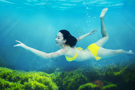 亮黄色的泳衣年轻女人在水下游泳背景
